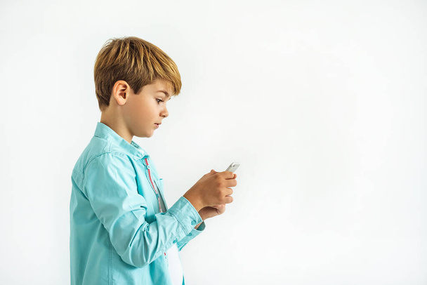 De kleine jongen met een telefoon op de witte achtergrond - Foto, afbeelding