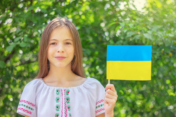 Nettes Mädchen in einem bestickten Volkshemd mit einer ukrainischen Flagge in den Händen. Konzept des Unabhängigkeitstages der Ukraine, Nationalfeiertage und Patriotismus. - Foto, Bild