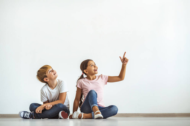 El niño feliz y una chica sentada en el suelo y mostrando en la pared - Foto, imagen