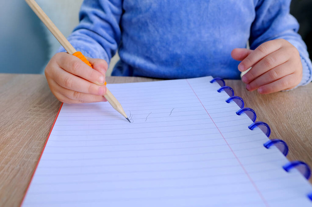 smart little child, girl in blue t-shirt, writes letters in notebook with an pencil, education concept, elementary school, hand development, developing writing skills - Photo, image