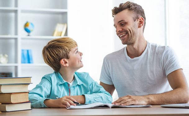 Счастливый отец и сын делают домашнее задание за столом - Фото, изображение