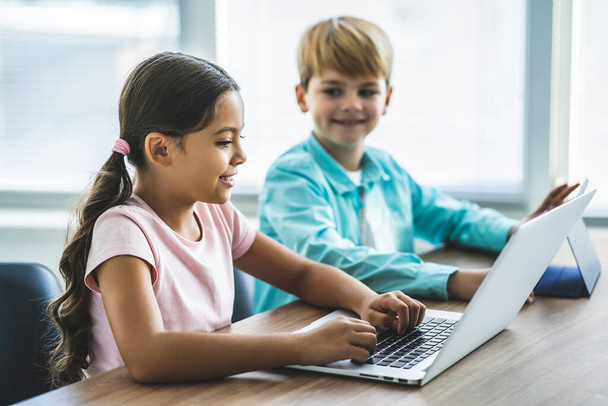 Chlapec a dívka s laptopem sedící u stolu - Fotografie, Obrázek