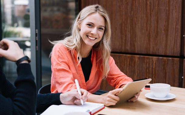 Portrait of blonde cheerful female student enjoying spending coffee break with male colleague, cropped image of positive woman looking at camera satisfied with free time on date with hipster guy - Photo, image