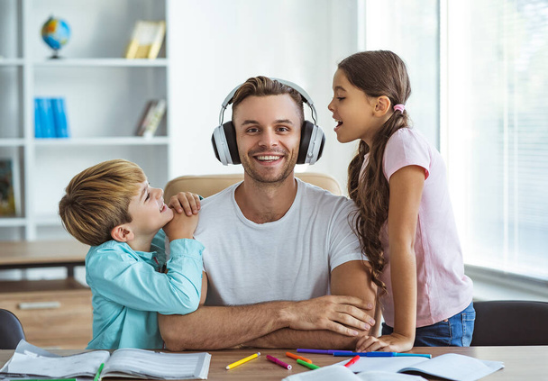 Ο χαρούμενος πατέρας με τα ακουστικά που παίζει με τα παιδιά στο γραφείο. - Φωτογραφία, εικόνα
