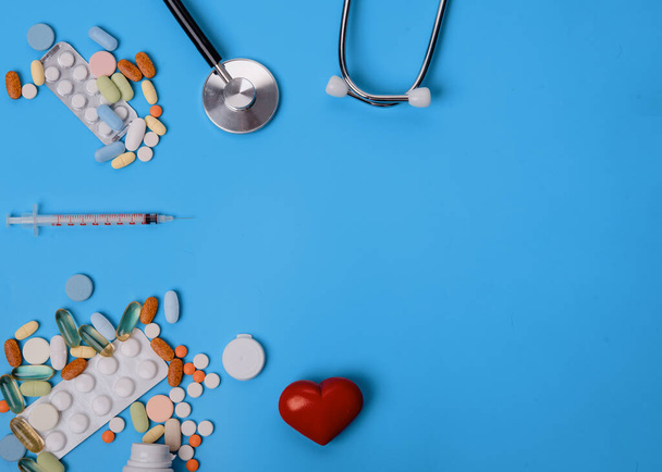 medische stethoscoop, pillen, hart en wegwerpspuit op blauwe achtergrond - Foto, afbeelding