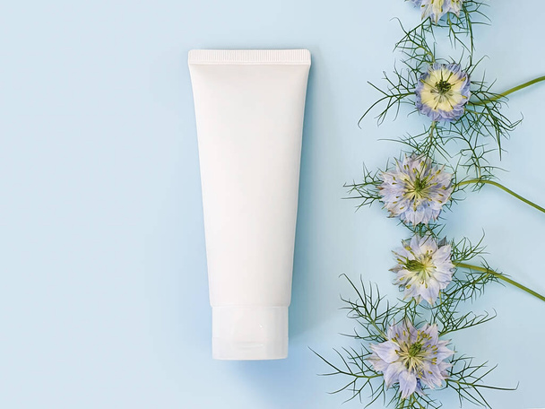 Unbranded white squeeze bottle cosmetic cream tube and line frame border of blue Nigella flowers on pastel blue background. Plastic tube for branding of medicine or cosmetics - shampoo, gel, skin care - Photo, Image