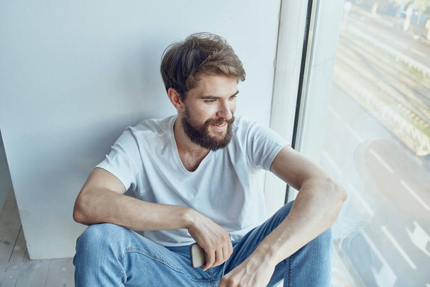 fehér pólós férfi ül az ablak mellett fülhallgatóban zenét hallgatva - Fotó, kép