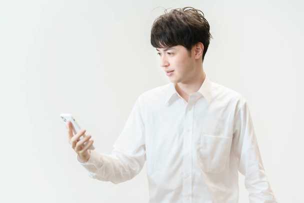 アジアの若い男はボーッとした状態でスマートフォンを見て - 写真・画像