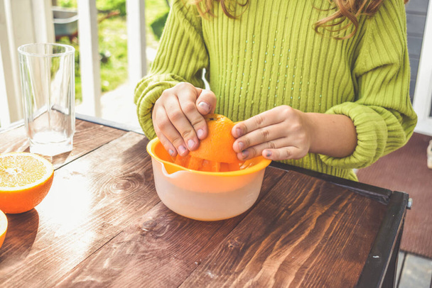 a girl child makes freshly squeezed orange juice on a manual juicer - Fotoğraf, Görsel