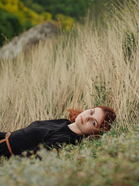 red-haired woman lies on the grass in the field rest fresh air - Foto, afbeelding