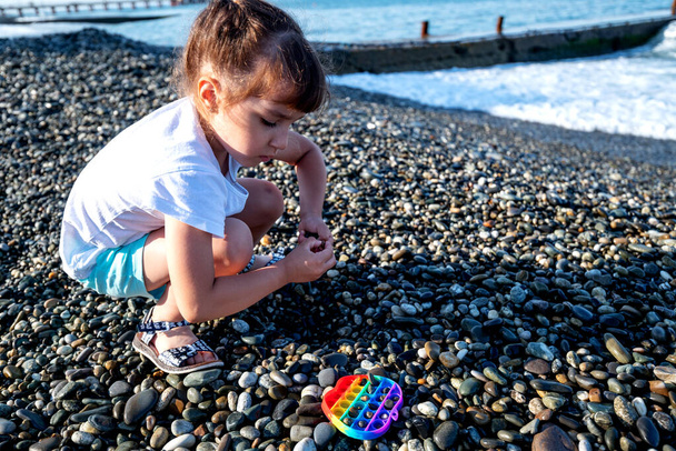 Девушка в шортах и футболке играет на камнях на берегу моря и лопает его ранним летним утром. - Фото, изображение