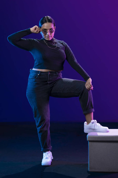 portrait latin woman posing in studio with a blue background wearing glasses and casual black clothes - Photo, Image
