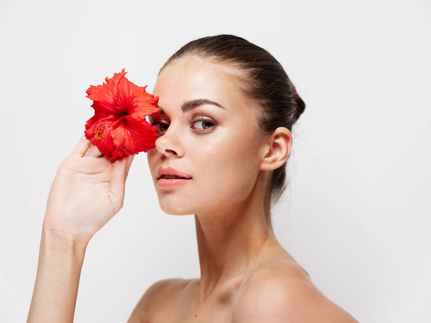 woman with red flower in front of eyes naked shoulders clear skin model - Photo, Image