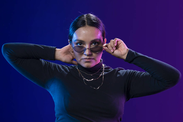 Portrét latinsky žena drží své brýle s modrým pozadím s fialovou - Fotografie, Obrázek