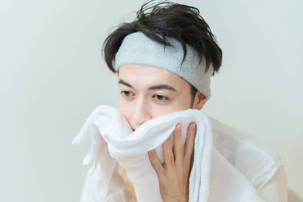 Ασιάτης νεαρός σκουπίζει το πρόσωπό του με μια πετσέτα - Φωτογραφία, εικόνα