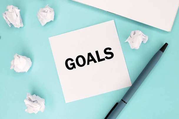 The word of the goal is written on a piece of paper that lies on a blue background near the crumpled sheets and a notebook. Business and educational concept - Photo, Image