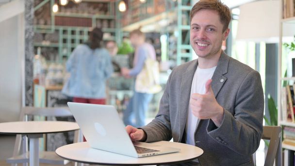 Thumbs Up by Young Man with Laptop in Cafe  - 写真・画像