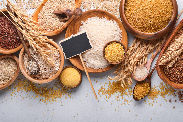 White, brown and red rice, buckwheat, millet, corn groats, quinoa and bulgur in wooden bowls on the light gray kitchen table. Gluten-free cereals. Top view with copyspace - Foto, Imagem