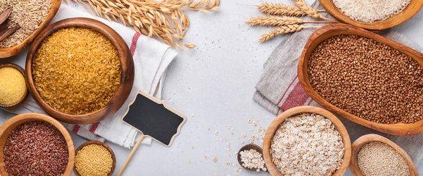 White, brown and red rice, buckwheat, millet, corn groats, quinoa and bulgur in wooden bowls on the light gray kitchen table. Gluten-free cereals. Top view with copyspace - Foto, Imagen