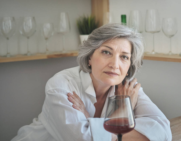 Ältere kaukasische Frau genießt ein Glas Rotwein und erinnert sich an angenehme Momente - Foto, Bild