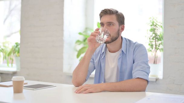 Молодий чоловік п'є воду в сучасному офісі
  - Фото, зображення