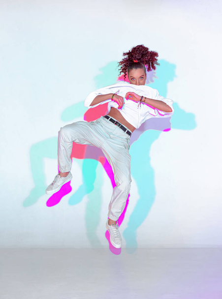 Dancing mixed race young girl in colourful neon studio light. Female dancer performer jumping hip hop dance - Foto, Imagen