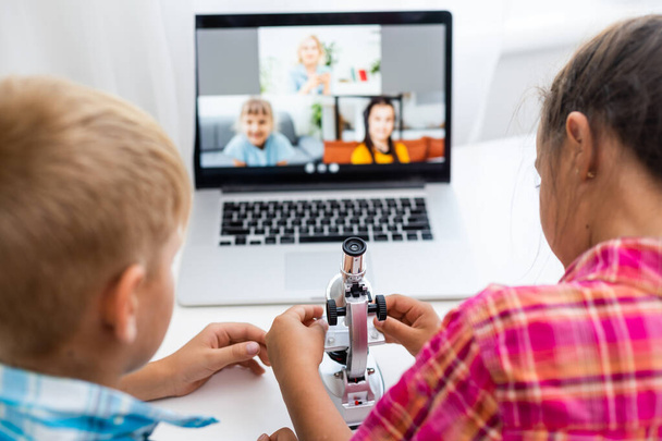 Junge und Mädchen, Bruder und Schwester lernen zu Hause. Ein Mädchen schaut sich eine Videostunde oder eine Online-Konferenz an, ein Junge macht Übungen in einem Notizbuch aus einem Lehrbuch - Foto, Bild