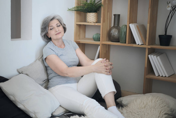 Liegende lächelnde ältere Frau, die sich auf einem bequemen Sofa ausstreckt, ruhig, meditierend - Foto, Bild