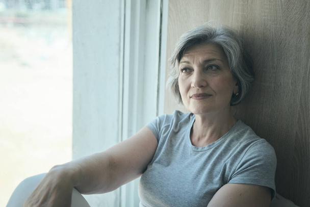 Пенсійна літня жінка в реабілітаційному центрі сидить біля вікна
 - Фото, зображення