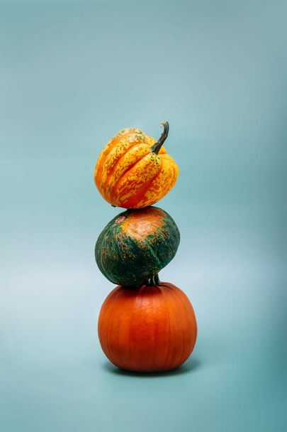 A tower made of decorative colorful pumpkins on the green-blue turquoise background. Autumn, fall, Halloween, Thanksgiving day concept. Minimalism. Vertical card. - Fotografie, Obrázek
