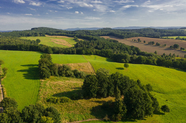Sudeten foothills. Undulating terrain covered with arable fields, meadows, clumps of trees. In the distance you can see mountains on the horizon. Photo from the drone. - Fotoğraf, Görsel