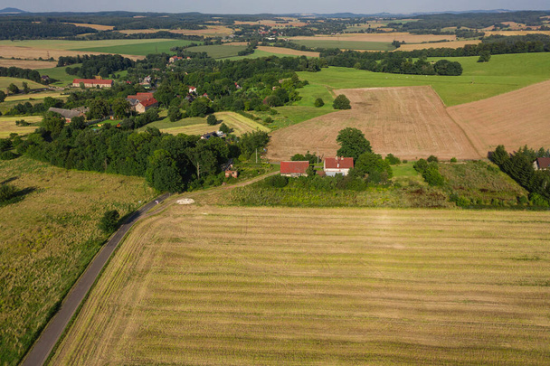 Sudeten foothills. Undulating terrain covered with arable fields, meadows, clumps of trees. In the distance you can see the buildings of the village and mountains on the horizon. Photo from the drone. - Fotografie, Obrázek