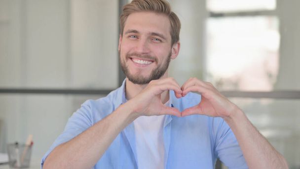 Πορτρέτο του νεαρού άνδρα που δείχνει το σημάδι καρδιάς με το χέρι  - Φωτογραφία, εικόνα