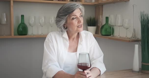 Ritratto di anziana donna felice con bicchiere di vino in un appartamento luminoso e confortevole - Filmati, video