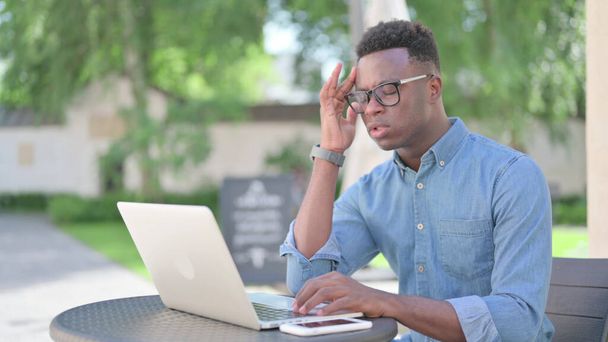 Afrikaanse man met laptop met hoofdpijn buiten - Foto, afbeelding