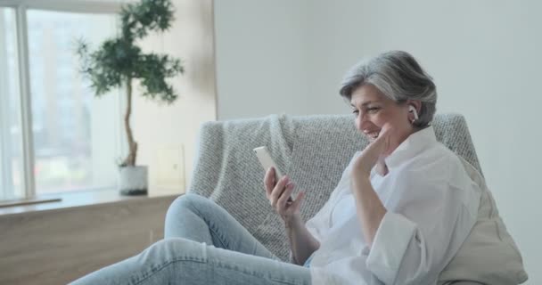 Felice anziana donna anziana in cuffia guardando schermo mobile, godendo di video incontro - Filmati, video