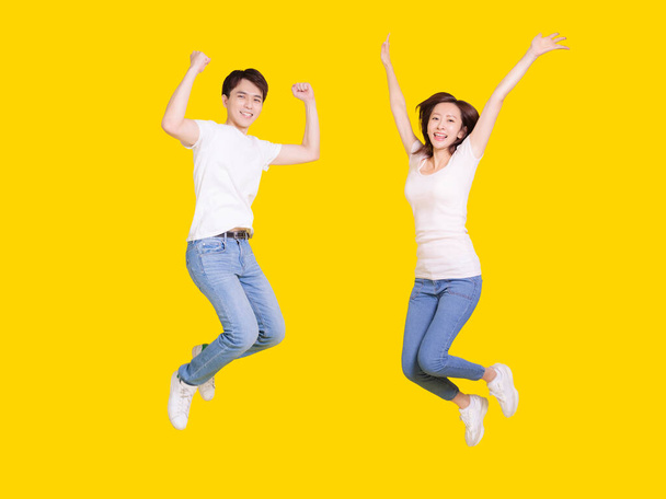 Ευτυχισμένο ζευγάρι άλμα.Νεαρός άνδρας και γυναίκα διασκεδάζουν μαζί.Απομονωμένο πάνω από κίτρινο φόντο. - Φωτογραφία, εικόνα