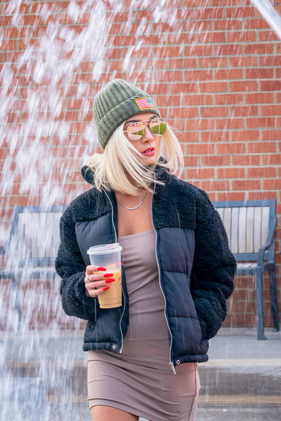 Sarışın, güzel bir manken, kış günü şehir ortamında kahvesini içerken dışarıda poz veriyor. - Fotoğraf, Görsel