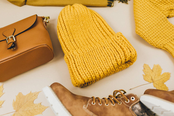 オレンジ革の女性のバッグ、ニットセーター、帽子、ブーツ、秋の葉ベージュ茶色の背景。トレンドの秋のアクセサリー。格好いい服 - 写真・画像