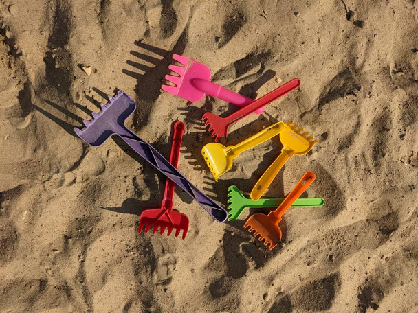 Egy rakás színes gyerekgereblye a homokban. illusztráció a közmondás lépés ugyanazon gereblye - Fotó, kép