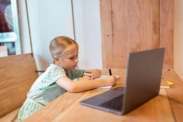 happy caucasian kid has online lesson on laptop during coronavirus covid-19 pandemic and lockdown - Φωτογραφία, εικόνα