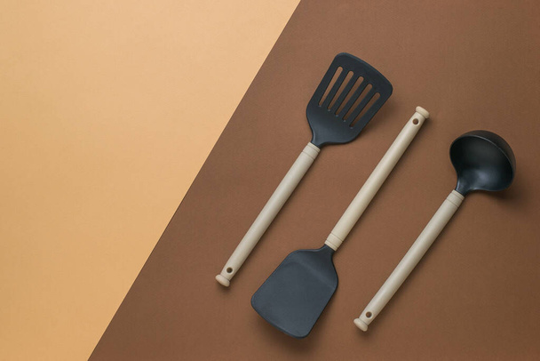 Tres utensilios de cocina sobre un fondo marrón bicolor. Herramientas de cocina de plástico. Puesta plana. - Foto, Imagen