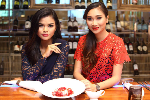 Zwei Bürofrauen essen im Restaurant auf Dating zu Abend. 20er Jahre junge Lovely Friends tragen blau roten formellen Anzug Kleid Umarmung zusammen auf Dinner-Set über Glas Likör Wanddekoration Raum, Kopierraum - Foto, Bild