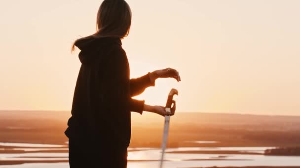 Junge Frau mit langen Haaren schwingt eine Klinge auf einem leuchtend orangefarbenen Sonnenuntergang und wirft sie in die Luft - Filmmaterial, Video