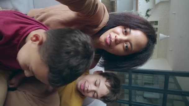 Close-up verticale video portret van een gelukkige Afro-Amerikaanse vrouw met een mobiele telefoon in uitgestrekte armen, zachtjes knuffelen haar schattige zonen en kijken naar webcamera terwijl het hebben van video call. - Video