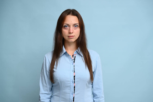 an adult woman bank worker in a blue shirt stands straight in a business pose on a blue background - Valokuva, kuva