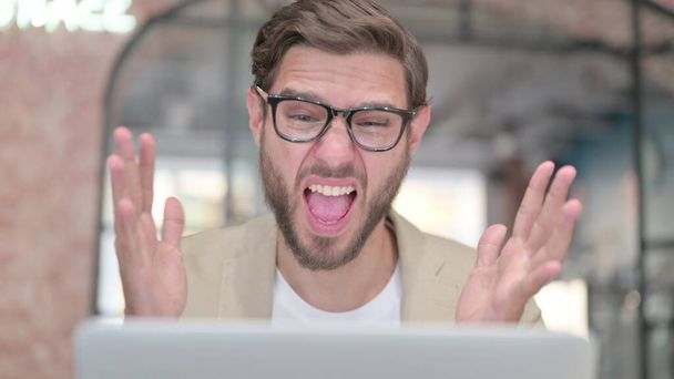 Νεαρός με φορητό υπολογιστή σοκαρισμένος στη δουλειά  - Φωτογραφία, εικόνα