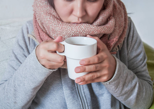 A young woman has a cold and drinks medicine. Autumn is the time of colds. The girl her throat with a scarf and drank hot. Treatment with folk remedies. On a winter evening, warm up with hot cocoa. - Fotoğraf, Görsel