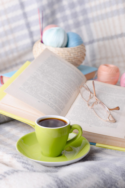 Cup of coffee and yarn for knitting on plaid with books close-up - 写真・画像