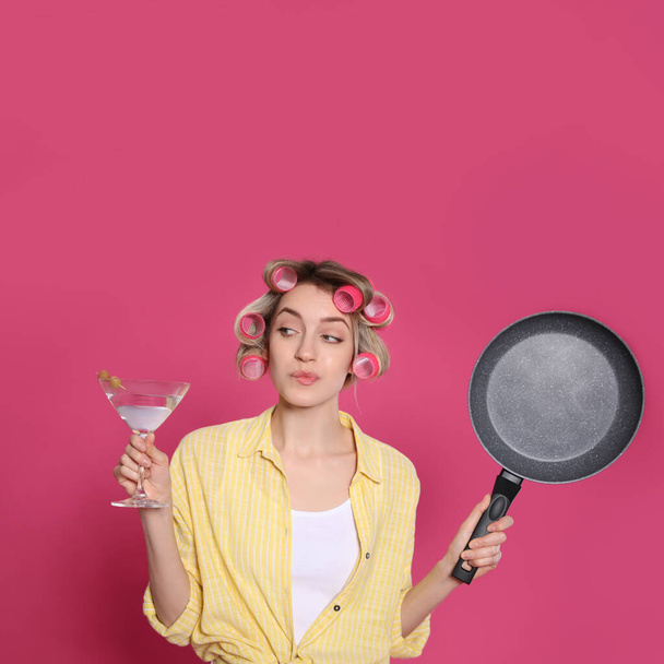 Young housewife with frying pan and glass of martini on pink background - Zdjęcie, obraz